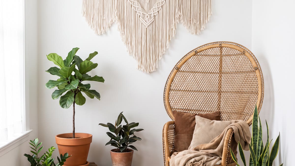 Esquina de oficina boho con macramé de pared, silla de rattán, escritorio de madera clara, plantas verdes y textiles cálidos