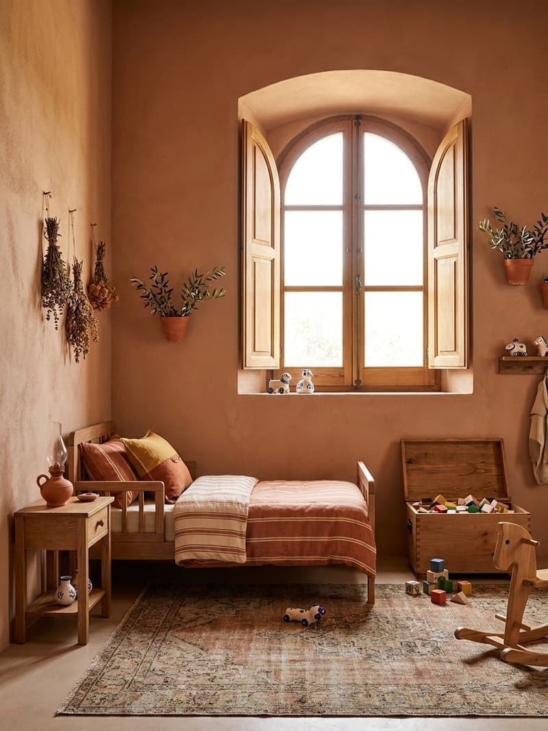 Habitación infantil mediterránea con cama de madera, ropa de cama terracota, persianas de madera y juguetes de madera vintage